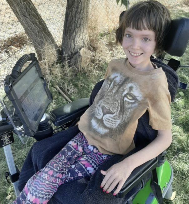 young girl in wheelchair with communication device mounted to wheelchair