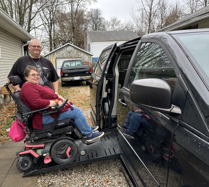 Mike and Lisa Overbay posing with their accessible van and Lisa is on the wheelchair ramp